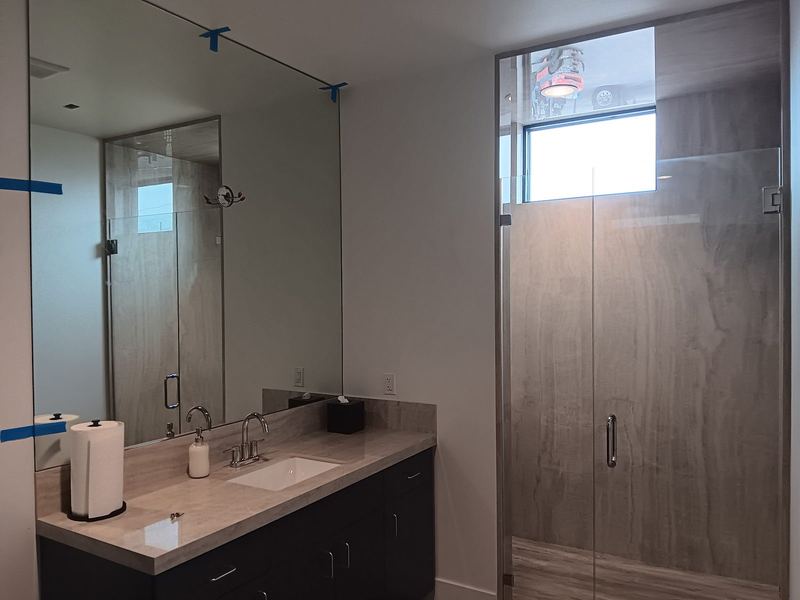 A finished frameless glass shower enclosure beside a full width vanity mirror