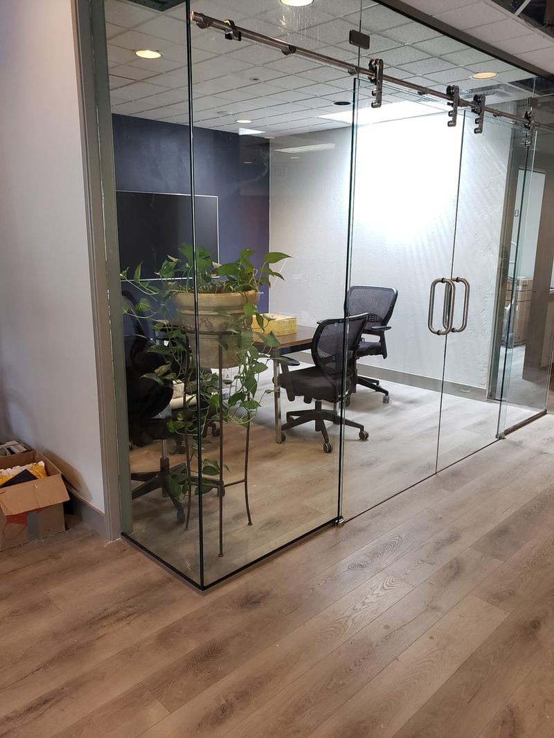 A frameless glass conference room front with sliding glass doors on exposed black track hardware