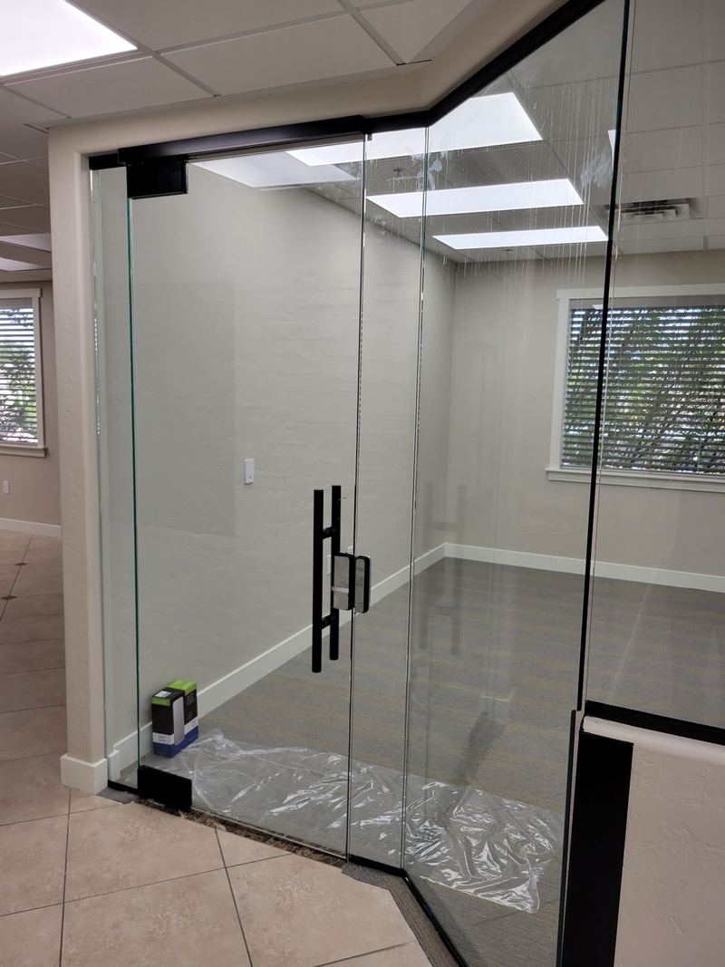 A frameless glass office entry with a full height black pull handle