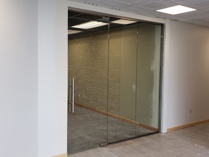 A full height glass partition wall with an integrated glass door dividing an office space