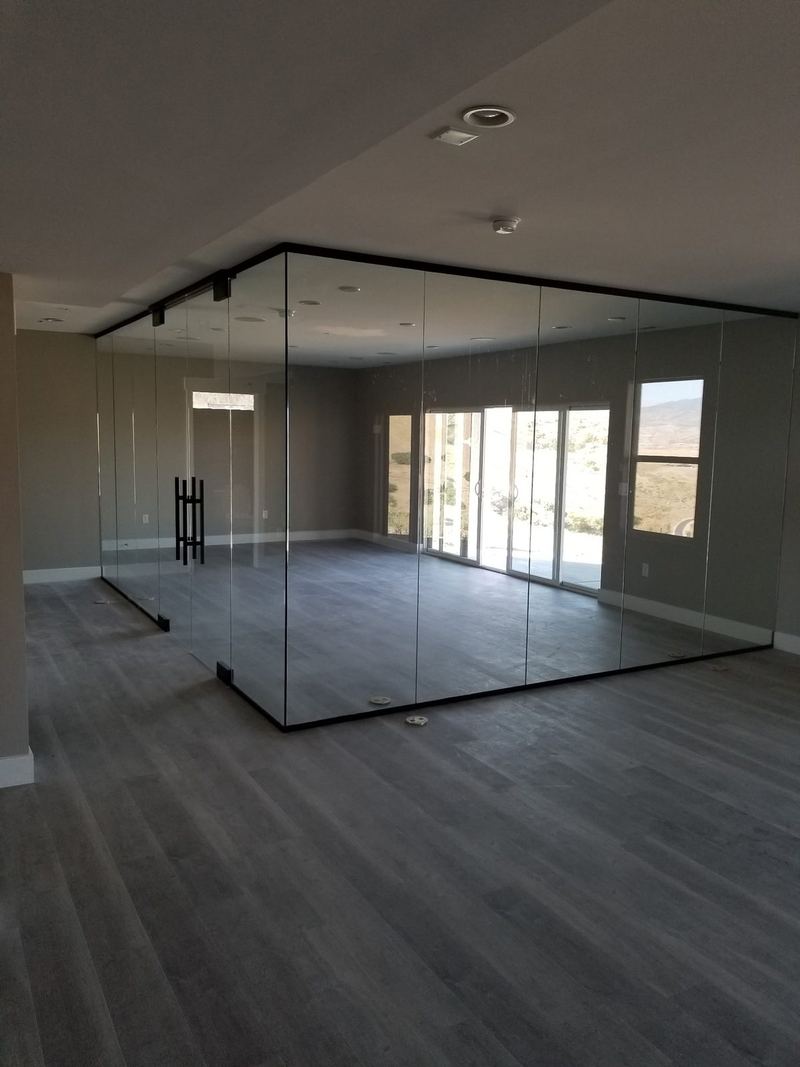 An empty office suite enclosed by dark framed glass walls with a corner return