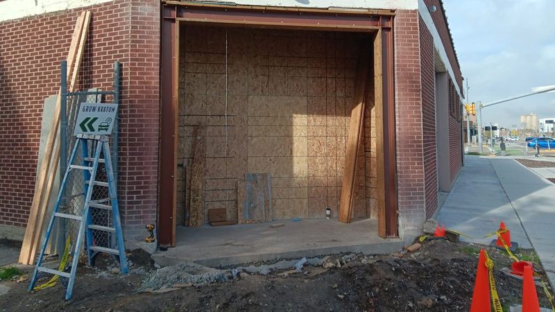 A commercial storefront opening framed and unglazed with a ladder propped against the brickwork