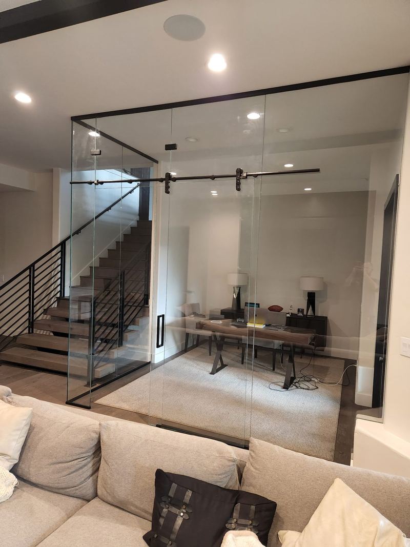 A glass enclosed home office with sliding glass doors on exposed track