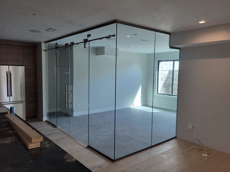 A glass walled room with sliding glass doors on exposed track hardware beside a kitchen