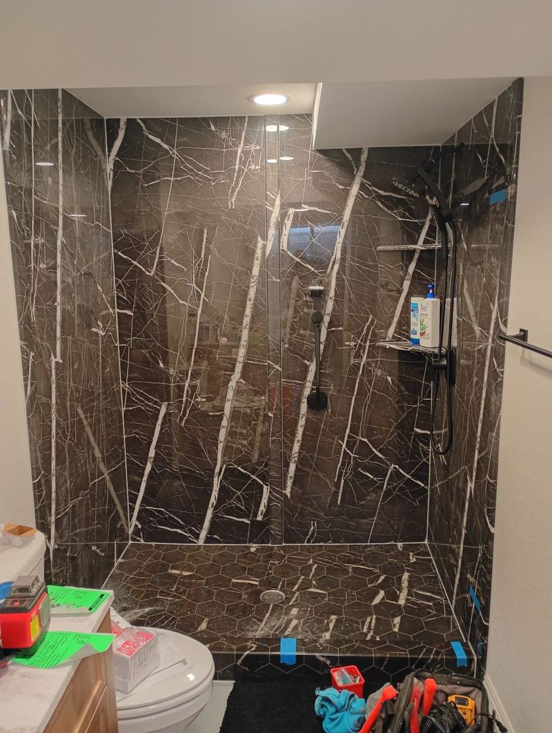 A tiled shower alcove in dark marble with no glass fitted and tools still on the floor