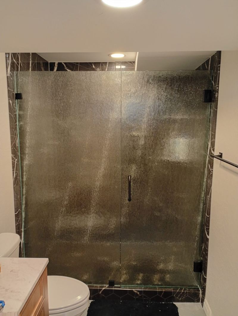 The same shower alcove fitted with a frameless glass enclosure and black hardware