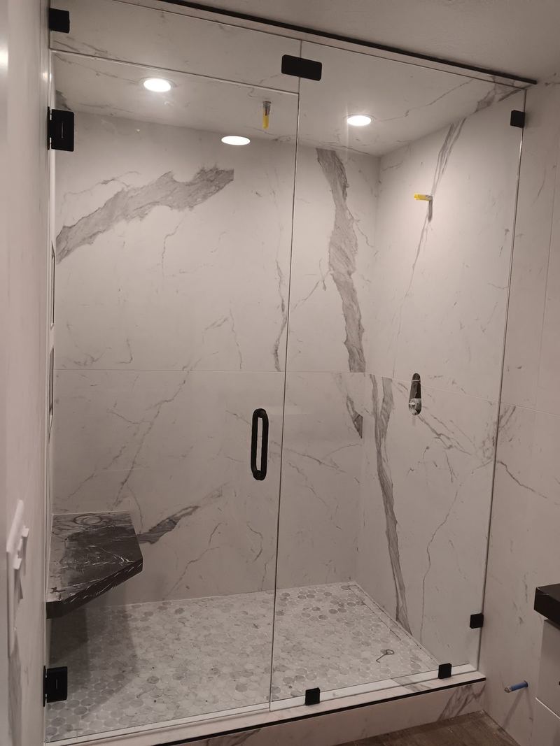 A frameless glass shower enclosure with black hardware and a marble bench seat