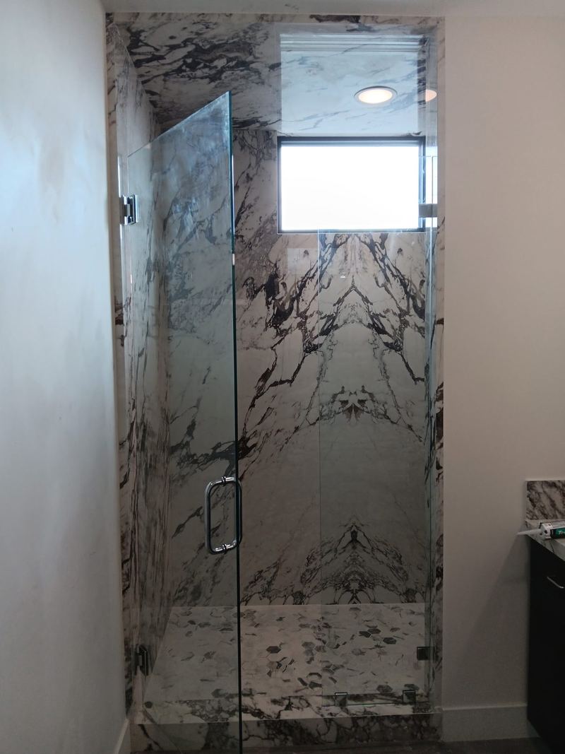 A frameless marble shower enclosure with a chrome handle